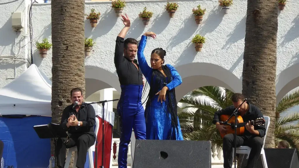 Cantaores y bailaores flamencos actuando en una plaza al aire libre acompañados de guitarrista.